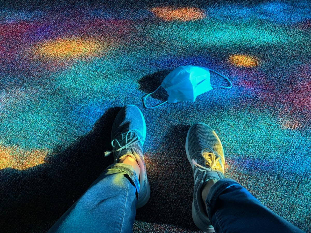 photo of feet with stained glass reflection on the floor and a mask on the ground